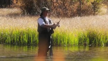 4K yaz gününde su geçirmez pantolonlu bir adam balıkçı oltası hazırlıyor.