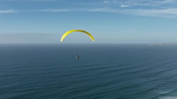 Luchtbeelden van een paraglider die boven de kust door de zee vliegt — Stockvideo
