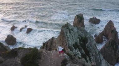 Yakışıklı beyaz erkek turist, yeşillikle kaplı bir pelerinin ucunda duruyor.