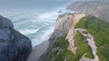 İnsansız hava aracı engebeli bir kıyı şeridini ve dalgaların kayalık bir sahile çarptığını gösteriyor.