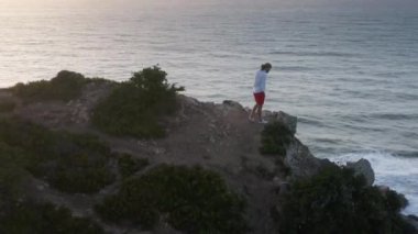 Erkek turist yaz tatilini kayalık bir pelerinin ucunda geçiriyor.