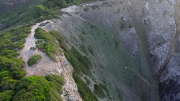 Paseos turísticos masculinos a lo largo de un acantilado rocoso y empinado con playa de arena debajo — Vídeo de stock