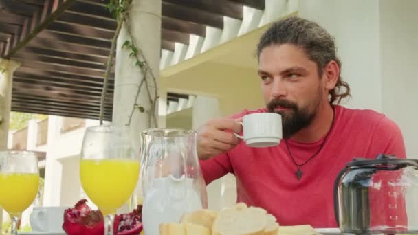 Adult caucasian male tourist enjoys his breakfast while sitting on a terrace — Stock Video