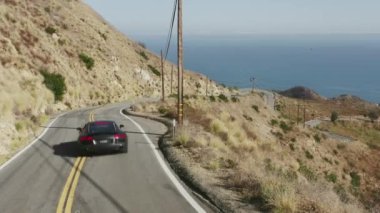 Malibu Kanyonu 4K 'da virajlı yoldan geçen siyah beyaz egzotik spor araba. 