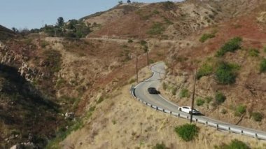 Malibu Kanyonu 4K 'da virajlı yoldan geçen siyah beyaz egzotik spor araba. 
