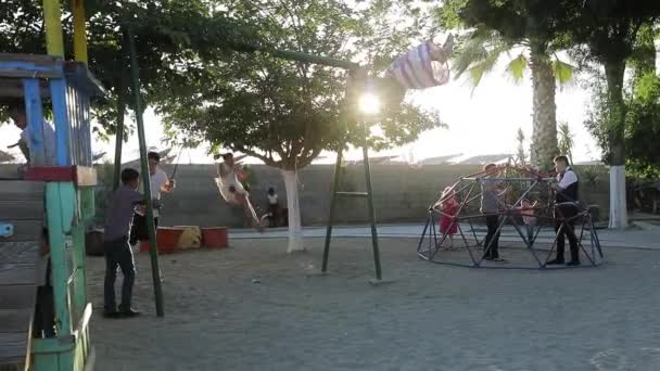 Детская площадка в солнечный летний вечер, счастливые беззаботные малыши, качающиеся — стоковое видео