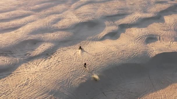 Aerial view of the people riding bike and buggy in harsh, uninhabited sand dunes — Stock Video