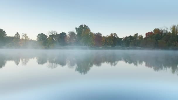 Niebla aérea de la mañana 4K sobre un lago quieto, niebla y vibrantes árboles de bosque rojo anaranjado — Vídeos de Stock