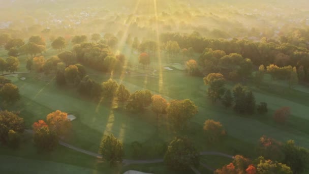 Zonnestralen breken door gouden mist boven landelijk dorp in herfstbos 4K — Stockvideo