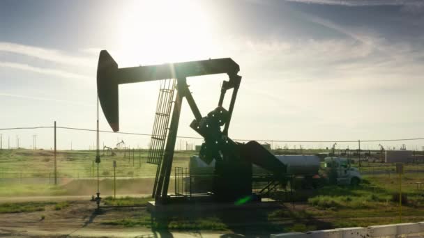 Нефтяной насос с зеленым ландшафтом на фоне сельской местности, нефтяная промышленность — стоковое видео
