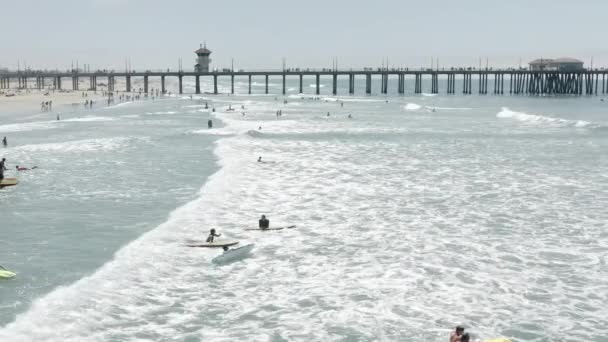 Серфингисты на насыщенном волнами участке побережья, покрытом пенным океаном — стоковое видео