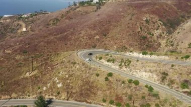 Egzotik, pahalı arabalar okyanus kıyısının yukarısındaki kıvrımlı dağ yılanbalığı yolunun yanından geçiyor. Yaz günü. Malibu Kanyonu 'ndan geçen hızlı arabalar Los Angeles, ABD 4K hız yarışı görüntüleri