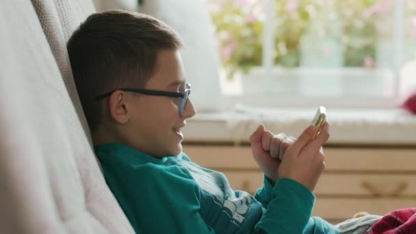 Side view of a schoolboy playing online games, while using his smartphone — Stock Video