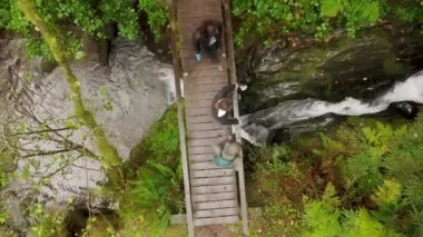 Nehir üzerinde ıslak, sinemalı ahşap köprü üzerinde yürüyen bir grup turist.