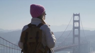 Kırmızı Golden Gate köprüsünü keşfeden, pembe şapkalı, ağır çekimli kadın. 