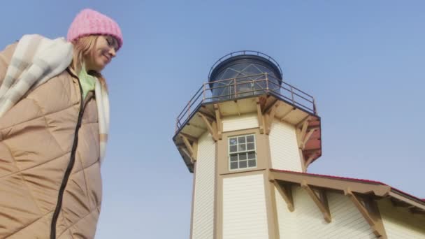 Plan à angle bas d'une jolie femme marchant autour de la tour du phare au lever du soleil 6K — Video