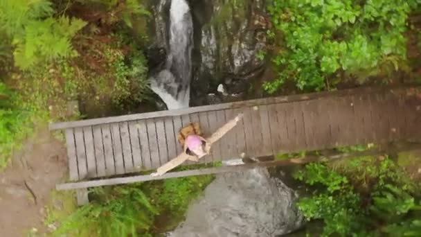 Ευτυχισμένη γυναίκα τουρίστρια περιστρέφεται με ανοιχτά χέρια σε ξύλινη γέφυρα κάτω από τη βροχή — Αρχείο Βίντεο