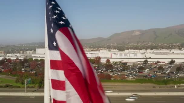 Drone aerial close up USA flag with Tesla factory on background 4K at sunset — стоковое видео