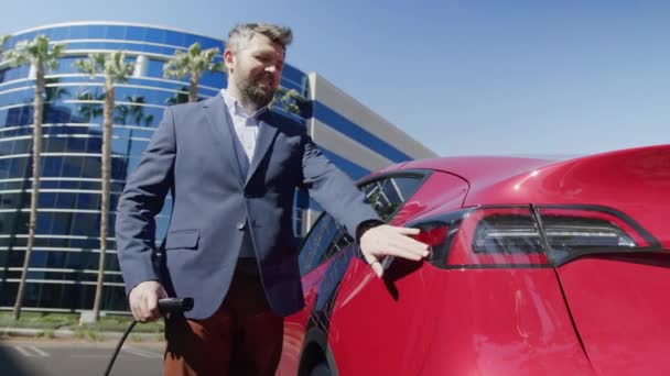 Senior zakenman is stekker in het netsnoer om elektrische auto op kantoor — Stockvideo