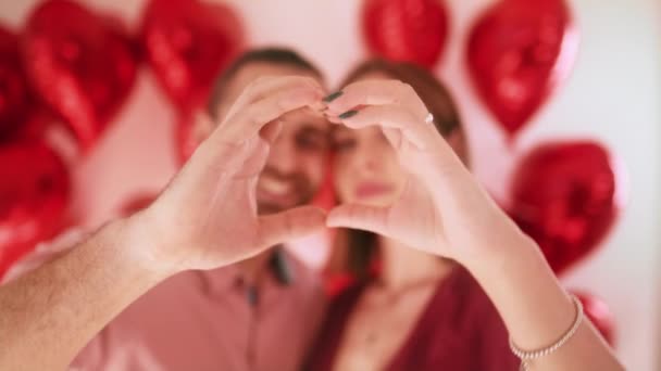 Закрыть портрет счастливая пара лиц, смотрящих сквозь пальцы, придавая форму сердцу — стоковое видео
