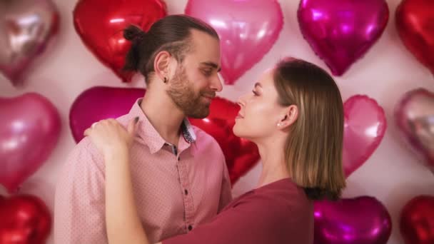 Positiv lächelndes verliebtes Paar umarmt stehend vor roter Herzballonkulisse — Stockvideo