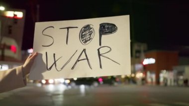 Kadın aktivistlerin yavaş çekimde yakın çekimde elinde WAR posteri var.