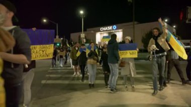 Sarı ve mavi Ukrayna bayrakları ve DUR SAVAŞ, DUR PUTIN işaretleri sallayan kalabalık