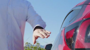 Adam, rüzgar jeneratörlerinin arka planında elektrikli bir arabayı şarja bağlıyor.