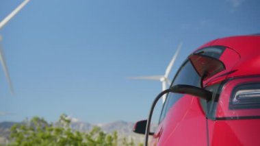 Güneşli yaz gününde hareket halindeki rüzgar türbinlerinin arka planında elektrikli araba, RED