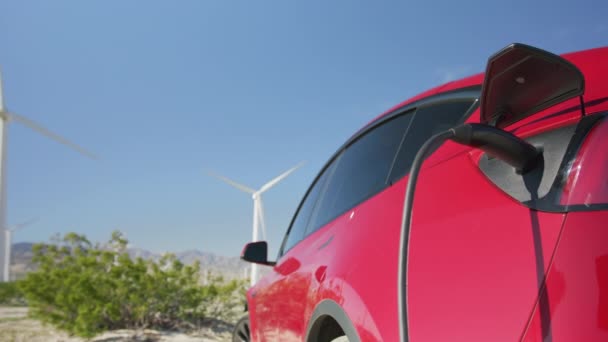 Generisches Laden von Elektroautos an einer Station in grüner Landschaft mit Windrädern — Stockvideo