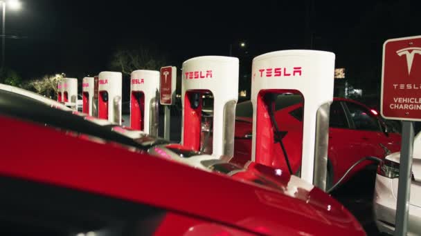 Медленное движение куклы Тесла электромобили подключены к зарядной станции на парковке — стоковое видео