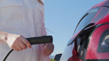 Kafkas kadın elinin kırmızı elektrikli arabanın şarj prizini açarken yakın plan çekimi.