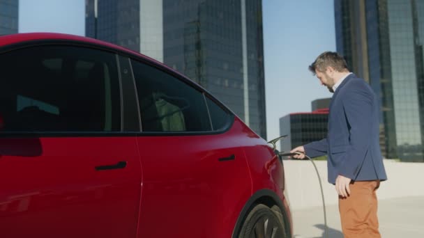 Vit affärsman med hjälp av smarttelefon väntar på att ladda elektriska fordon — Stockvideo