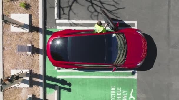 Overhead disparo joven mujer caucásica en la estación de carga de coches eléctricos en el día — Vídeo de stock