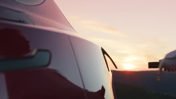 Wolno poruszająca się kobieta podłączająca przewód zasilający w 0-emisyjnym samochodzie elektrycznym o zachodzie słońca — Wideo stockowe