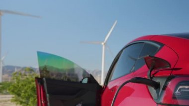 Adam elektrikli araba şarj kablosu 6K 'yı çekmek için modern kırmızı SUV arabasından iniyor.