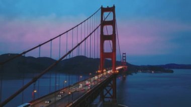 Aydınlatılmış Golden Gate Köprüsü 'nün hava manzarası, trafiğin üzerindeki pembe bulutlu gün batımı.