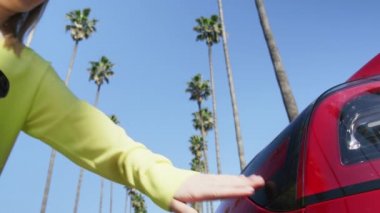 Avuç içlerindeki kırmızı elektrikli araba prizine şarj kablosu takan genç bir kadın.