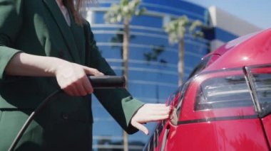 Şehir caddesindeki iş kadını modern kırmızı elektrikli SUV 'u şarj ediyor.