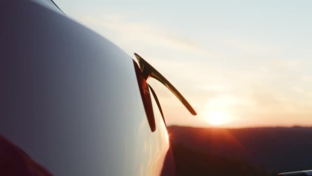 Невпізнаваний підприємець підключає електричний автомобіль зі станції заряджання на заході сонця — стокове відео