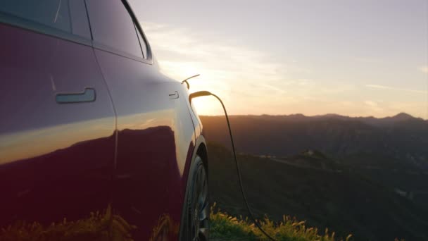 Dolly shot snoer opladen EV voertuig buiten bij schilderachtige gouden zonsondergang achtergrond — Stockvideo