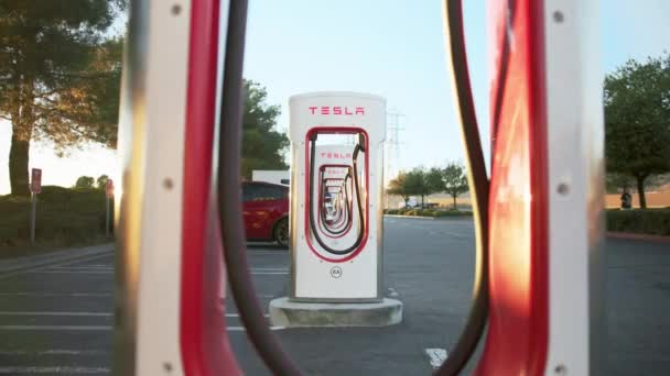 Dolly shot through white and red Tesla electric charging stations, golden sunset — Stock Video