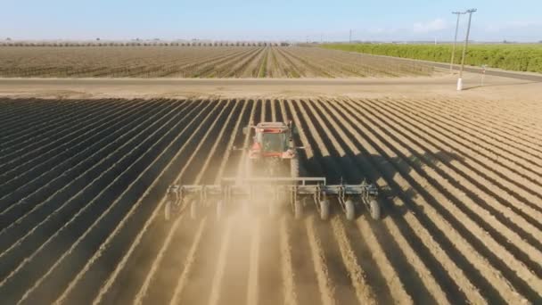 Вид с воздуха на трактор, вспахивающий местность, оставляющий мелкие канавы на суше — стоковое видео