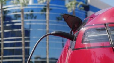 Yakın plan beyaz, mavi takım elbiseli yetişkin adam kırmızı araca şarj kablosu çekiyor.