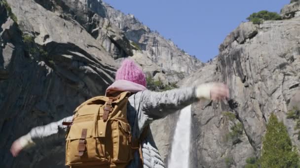 Mujer sonriente con mochila turística levanta los brazos en el aire, quitándose el sombrero rosa — Vídeos de Stock