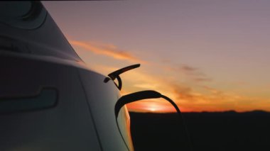 Ağır çekim kadın çevre dostu elektrikli araç günbatımından güç kablosunu çıkarıyor