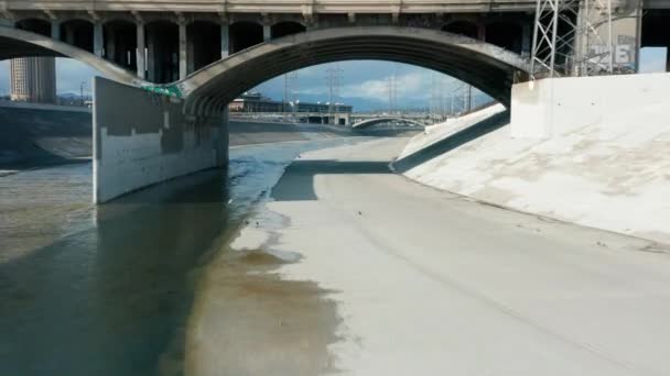 Drone flying under arched concrete bridge above scenic Los Angeles River water — 비디오