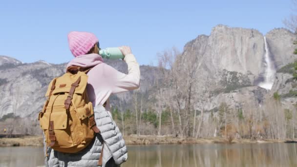 受到启发的年轻女子站在高山湖畔或河边，享受着热茶 — 图库视频影像