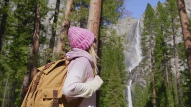 Yavaş çekim gülümseyen kadın, şelale manzaralı çam ormanının tadını çıkarıyor.