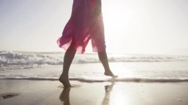 İnce kadın bacakları ve ayakları deniz dalgaları boyunca yürüyor kumlu kumsal kameraları